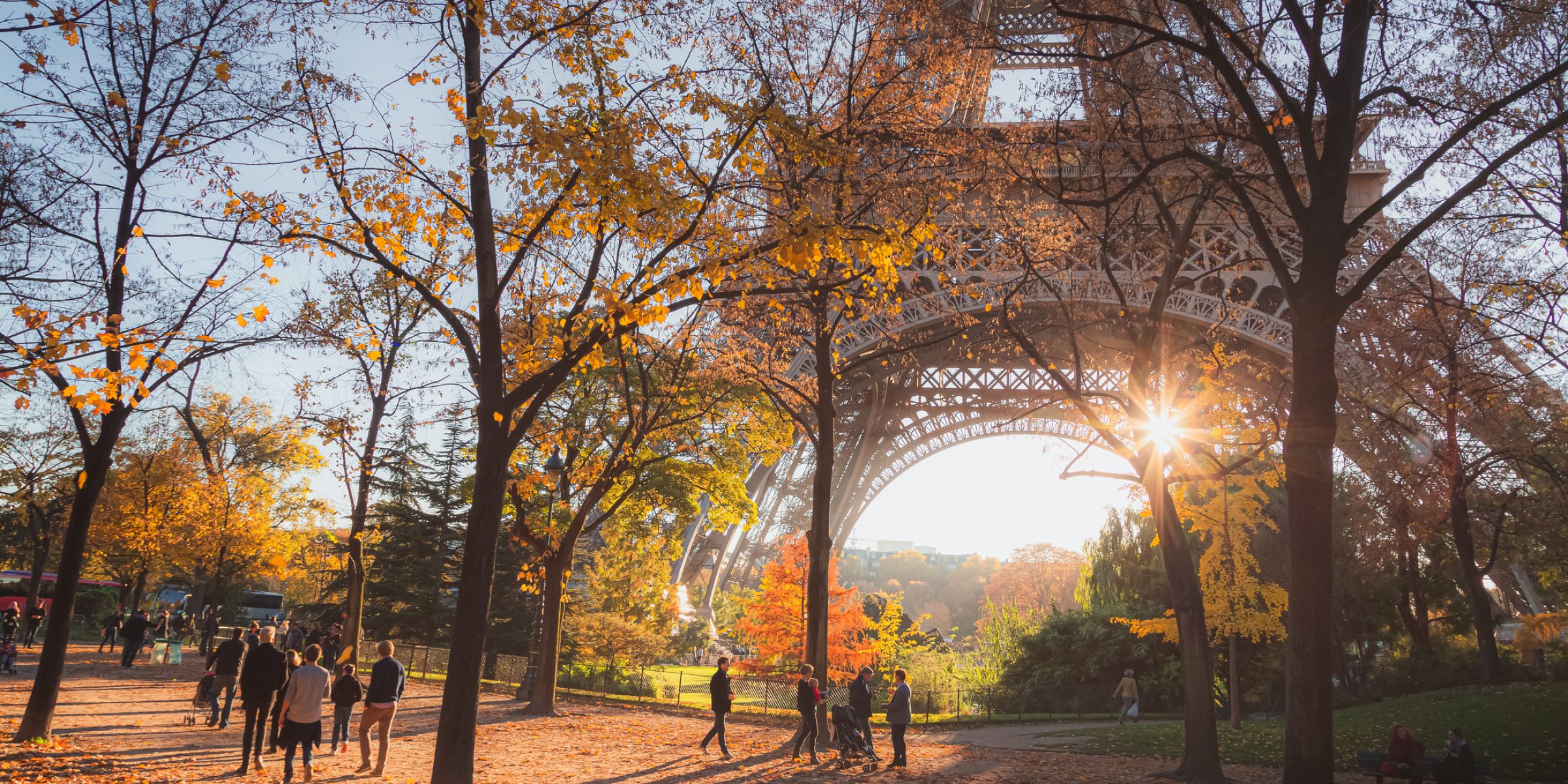 Tourists, locals and families enjoy a scenic autumn stroll as sunlight bursts through the iconic Eiffel Tower in Paris, France.