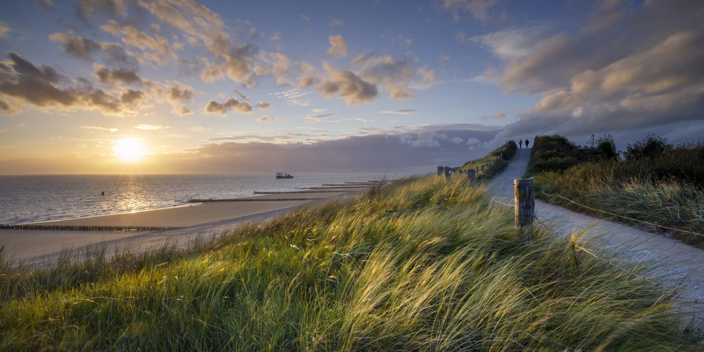 two people walking along the coastal path at sunset at the Zeeland coast near Zoutelande, North Sea
